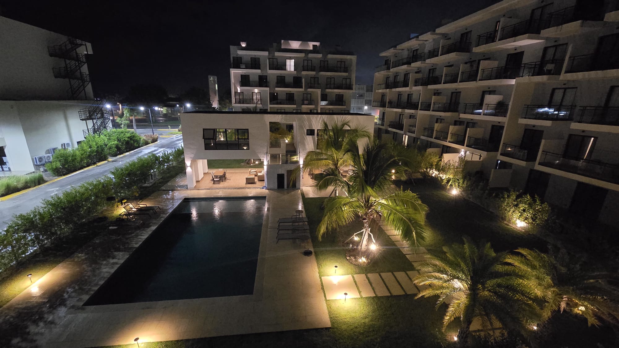 Residence pool and gardens illuminated at night with palm trees and apartments