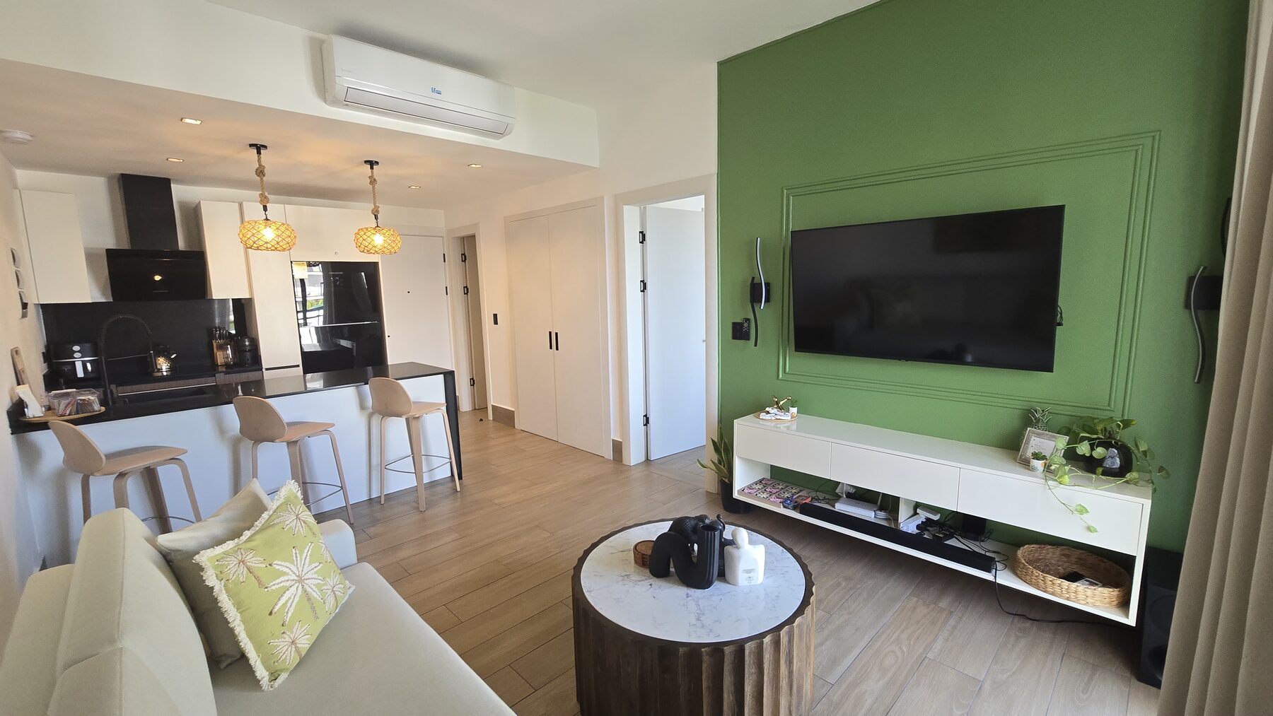 Living area with smart TV on a green feature wall and open kitchen behind